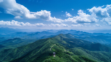 Naklejka premium Expansive Aerial Landscape: Green Mountain Range, Winding Path, and Blue Sky with Clouds