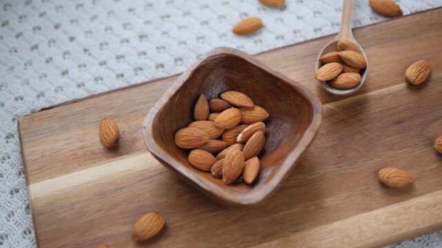 Slow motion footage of raw almonds being poured into a beautiful rustic wooden bowl placed on a cutting board, a perfect representation of healthy snacking and natural organic food