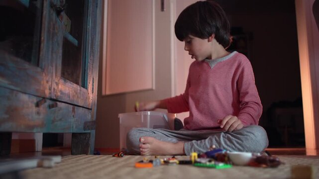 Young boy sitting on floor putting toys back into box, showing responsibility, focus, and early sense of order during calm evening at home