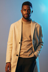 Stylish and confident Black man wearing a light beige coat and sweater, showcasing modern fashion against a soft blue and gray background