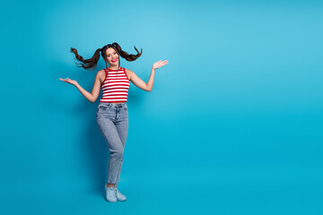 Young cheerful brunette woman in striped top and jeans with playful ponytails posing on a bright blue background