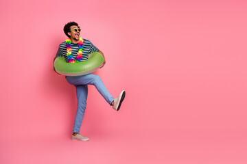 Young mixed race man with a green inflatable ring dancing in a pink studio smiling for casual lifestyle and fashion promotional image