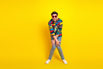 Fototapeta premium Young man in colorful patterned shirt wearing red sunglasses poses playfully against a bright yellow background for fashion lifestyle and advertising uses