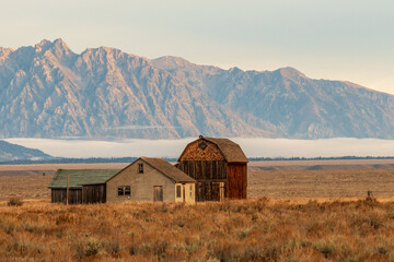 Home and a barn in the Mormon Row historic district with a low mist across the prairie and a mountain ridge from the Rocky Mountains in the background