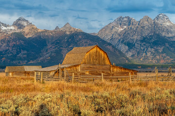 The iconic antique T.A. Moulton barn in Grand Teton National Park at Sunrise with Grand Teton and the snowcapped mountains of the Teton Range behind the field