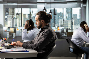 Business manager working on finance and budgeting at desk, consulting data archives and projections for development. Staff analyzing documents, diagrams and reports to meet goals.