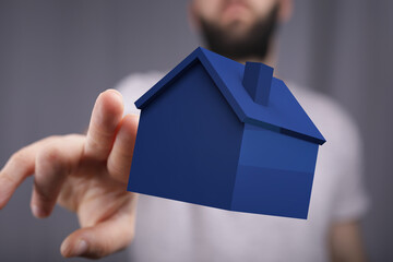 A person's hand reaching towards a blue house model, symbolizing real estate, property ownership,...