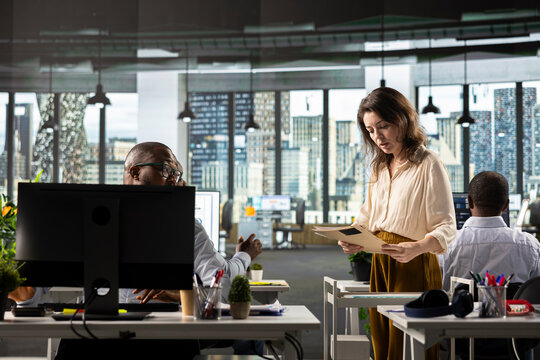 Female assistant giving files and reports from archive to worker in office, pushing trolley with multiple folders. Employees studying old insights for business intel and risk assessment.