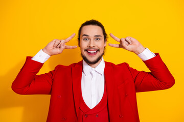 Playful stylish man in red suit says hello with peace signs on a bright yellow backdrop for bold...