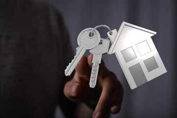 Close-up of a person's hand holding keys with a house-shaped charm, representing homeownership, property investment, and security. Perfect for r