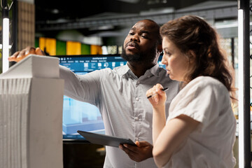 Diverse contractors gathering around 3D models and blueprints to study layout details, making site...