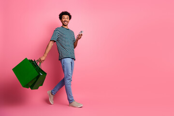 Young mixed race man with striped shirt walking with shopping bags against pink background smiling...