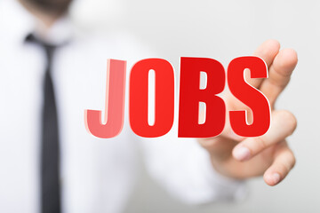 A businessperson's hand reaching towards the word JOBS, symbolizing career, employment, and job...