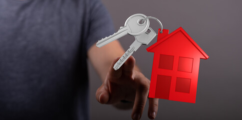 A person's hand offers keys attached to a red house, symbolizing home, real estate, property, and...