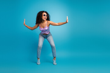 Obraz premium Young woman in purple top and jeans dances with open arms against blue background conveying energy confidence