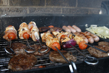 beef burgers, pork sausages & chicken kebabs cooking in the garden on a barbecue, tasty summer food outdoors 