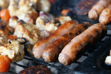 beef burgers, pork sausages & chicken kebabs cooking in the garden on a barbecue, tasty summer food outdoors 