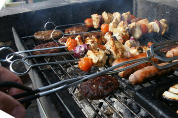 beef burgers, pork sausages & chicken kebabs cooking in the garden on a barbecue, tasty summer food outdoors 
