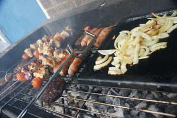 beef burgers, pork sausages & chicken kebabs cooking in the garden on a barbecue, tasty summer food outdoors 