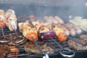 beef burgers, pork sausages & chicken kebabs cooking in the garden on a barbecue, tasty summer food outdoors 
