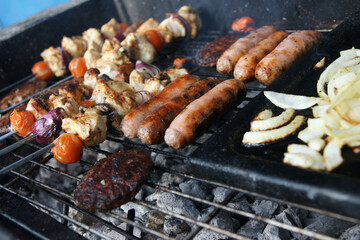 beef burgers, pork sausages & chicken kebabs cooking in the garden on a barbecue, tasty summer food outdoors 