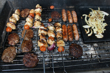 beef burgers, pork sausages & chicken kebabs cooking in the garden on a barbecue, tasty summer food outdoors 