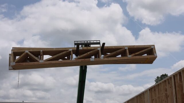 Worker stands on structure while using use telehandler crane to set wooden beams in place during works day