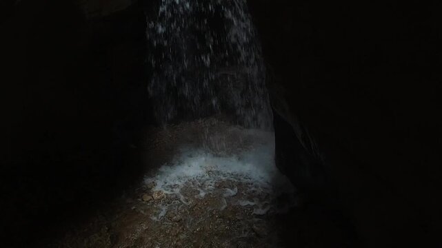 Extreme slow motion (240 fps) shot of water crashing down a hidden waterfall inside a narrow cave. Cold spray hits the rock in darkness, capturing raw force, danger, isolation and survival mood.