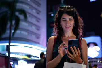 Woman smiling using smartphone at city night