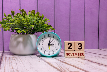 Wooden calendar organizer with date november 23 and decorative plant on table.