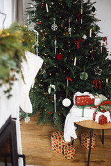 Stylish Christmas presents. Merry Christmas and Happy Holidays! Wrapped Christmas gift boxes on table at decorated xmas tree with lights in cozy room. Atmospheric winter time