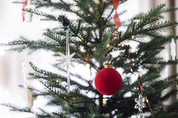 Red bauble and star on Christmas tree branches close up. Stylish holiday bauble and ornaments on decorated xmas tree with lights. Winter holidays decor, atmospheric christmas time