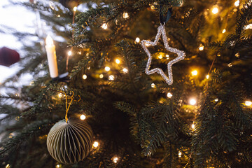 Star and bauble on Christmas tree branches close up in eve. Stylish holiday bauble and ornaments on...