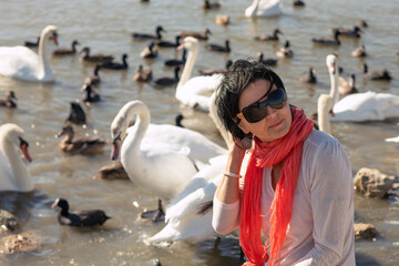 brunnet girl sitting near lake with white wild beautiful swans at sunny day. close up. Crimea,...
