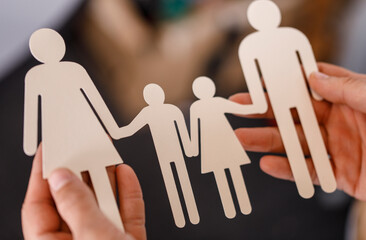 Close-up of paper figures representing a family, held by hands, symbolizing togetherness,...