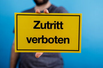 A hand holding a yellow sign in German that reads 'Zutritt verboten' meaning 'Access Prohibited' against a bright blue background.