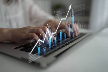 A close-up view of hands typing on a laptop with a digital financial graph displayed, representing...