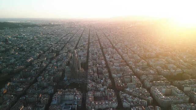 4K drone aerial view of Sagrada Familia in Barcelona at sunset, showing golden light over Eixample district and iconic grid city pattern, Catalonia, Spain
