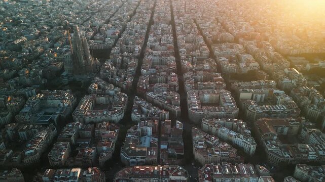 4K drone aerial view of Sagrada Familia in Barcelona at sunset, showing golden light over Eixample district and iconic grid city pattern, Catalonia, Spain