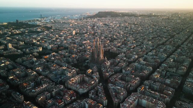 4K drone aerial view of Sagrada Familia in Barcelona at sunset, showing golden light over Eixample district and iconic grid city pattern, Catalonia, Spain
