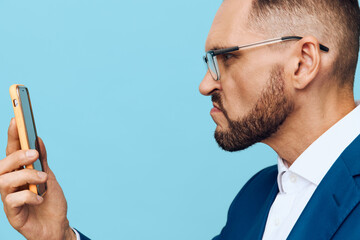 A focused businessman in a blue suit checks a mobile device against a solid light blue background, conveying professional mood, concentration, and deliberate emotion.
