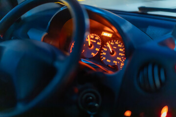 The illuminated dashboard of a car shows the speedometer, tachometer, and odometer display at night.