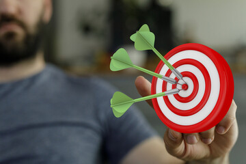 Image of a man holding a dartboard with darts hitting the bullseye, representing success, achieving...