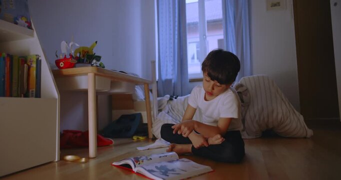 Boy sitting on bedroom floor reading book with focus, child concentrating on study and imagination, learning and concentration during early development at home