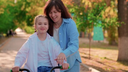 Mom teaches little daughter to ride bike in park. Child is learning to ride bike. Happy family, mother daughter. Child is riding bike for first time. Kid girl laughing smiling with her mom. Kid travel