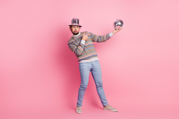 Cheerful young man in a colorful sweater posing with a disco ball against a pink backdrop for a vibrant and lively promotional image