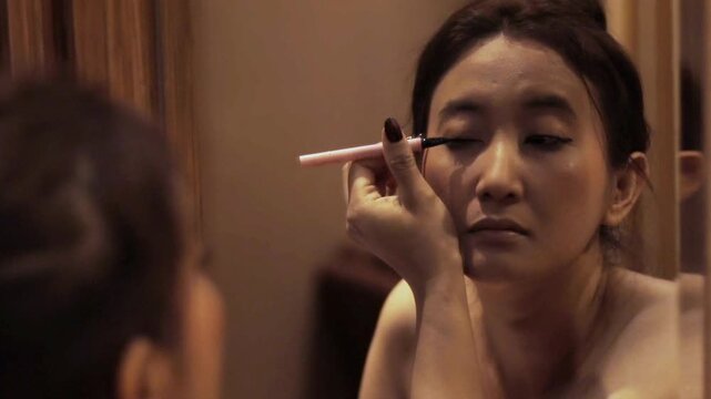 A woman applying eyeliner in front of a mirror, capturing the process of beauty routine for makeup tutorials or - Powered by Adobe