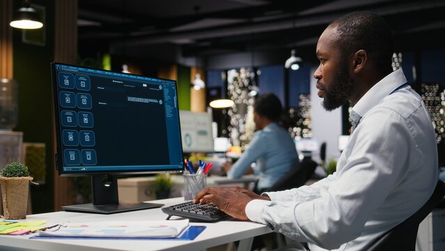 African american male checking web AI chatbot responses for some tasks, working after hours to meet business objectives. Problem solving with futuristic tech and machine learning.