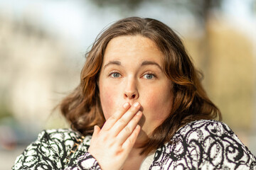 Surprised woman covering mouth with hand outdoors showing shock or amazement expression