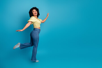 Obraz premium Joyful young woman posing playfully against a blue background wearing a casual yellow top and jeans
